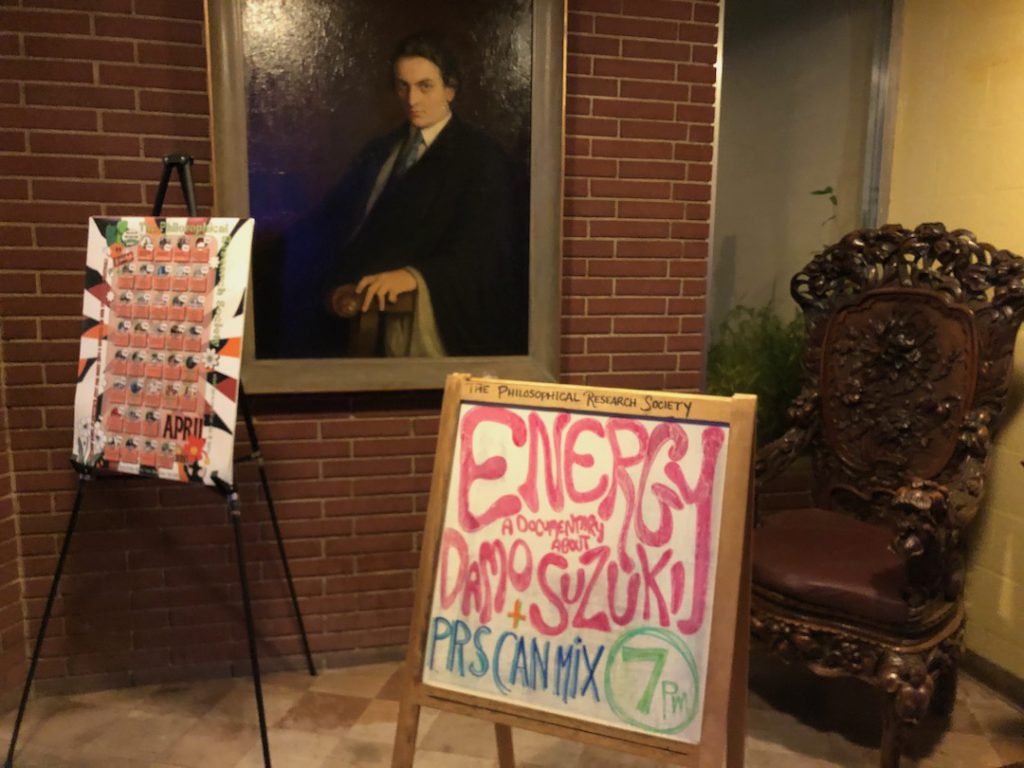 Auditorium lobby at Philosophical Research Society in Los Feliz, Los Angeles with sign for screeening of "Energy: A Documentary About Damo Suzuki" in foreground and portrait of Manly P. Hall in background.