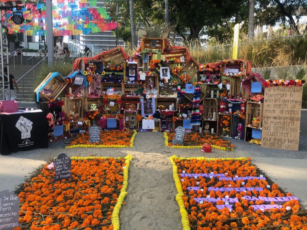 "Through Shadows of Sacrifice, Women Carried by Hope" by East Los Angeles Women's Center at Gloria Molina Grand Park. Large altar made of crates and filled with flowers, sugar skulls, photos and other mementos. (Photo: Liz Ohanesian)