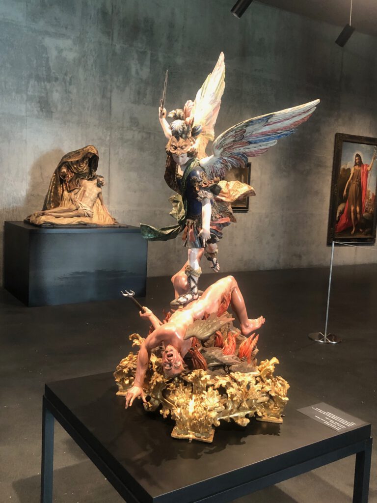 Statue of St. Michael casting satan into hell in the foreground (Francesco Picano and Lorenzo Vicaro) and a pieta from Spain the background at David Geffen Galleries. (Photo: Liz Ohanesian)